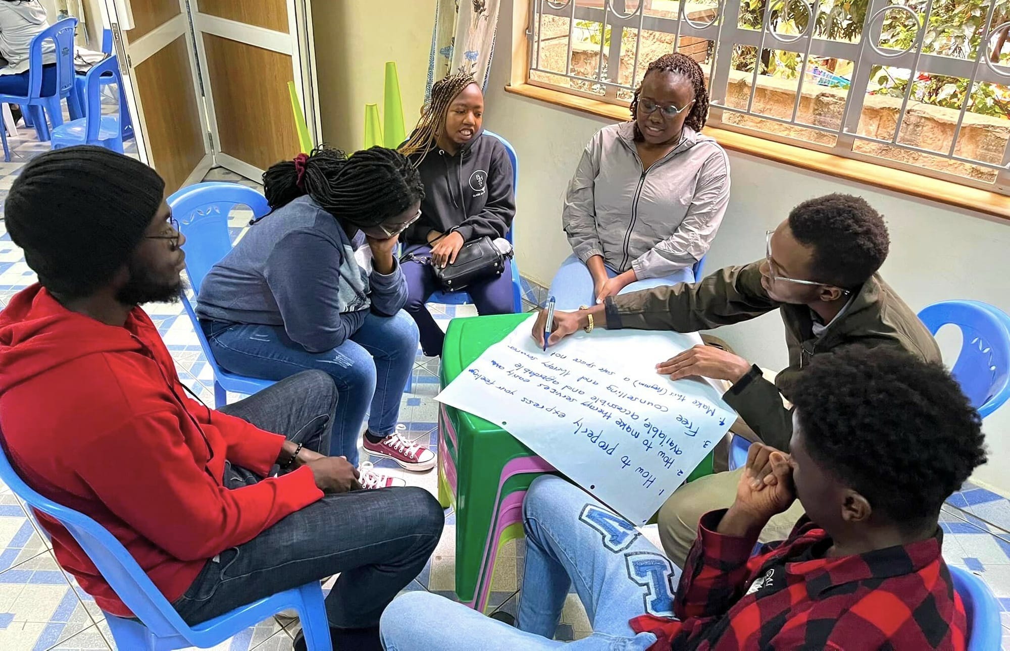 Image of a group of young people sitting around a circle, writing on a large sheet of paper