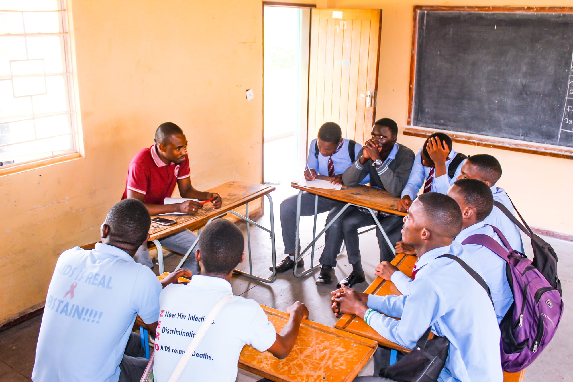 A group of young Zambian men gathered in a circle, with a facilitator dressed in red in the center engaging them