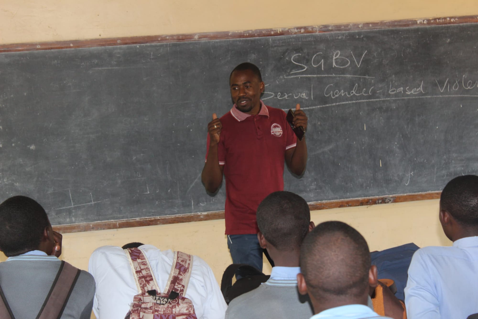 Image of a man in a red shirt standing in front of a classroom giving a thumbs up