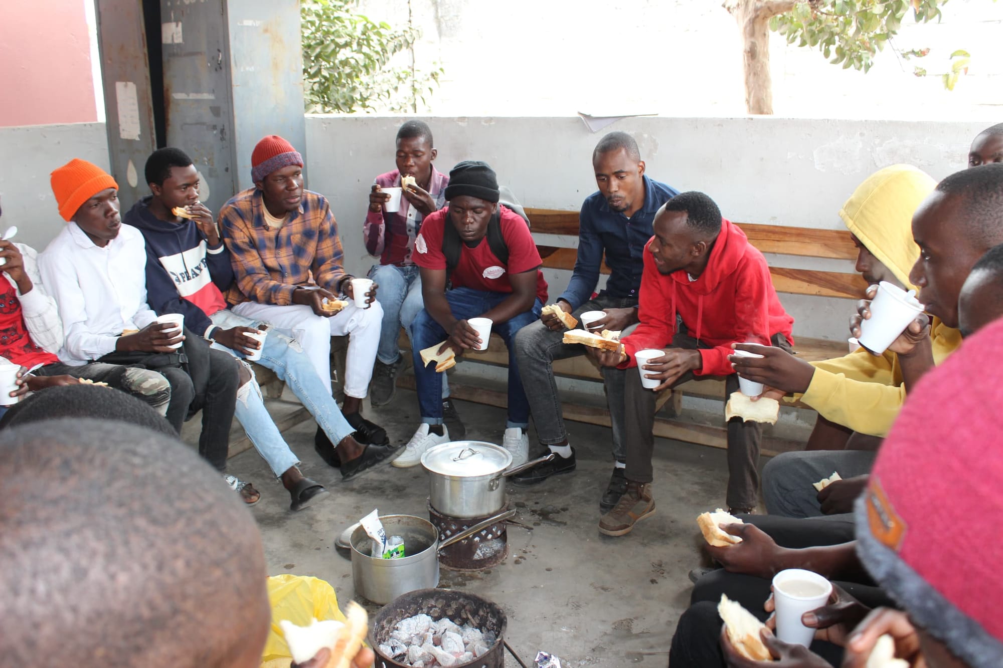 A group of Zambian men gathered in a circle, with a pot of food in the center