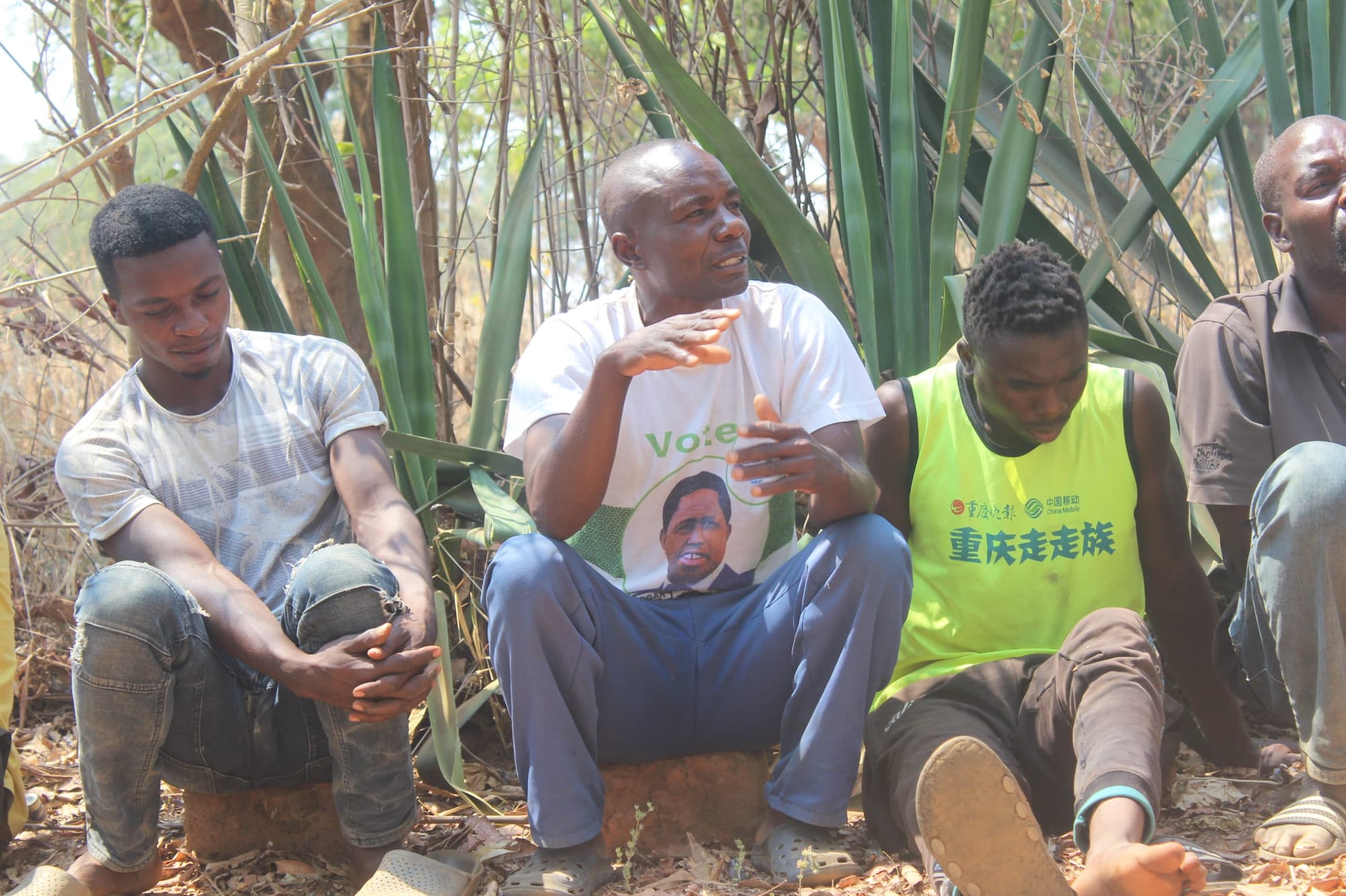 Four Zambian men sitting in a field engaged in a discussion